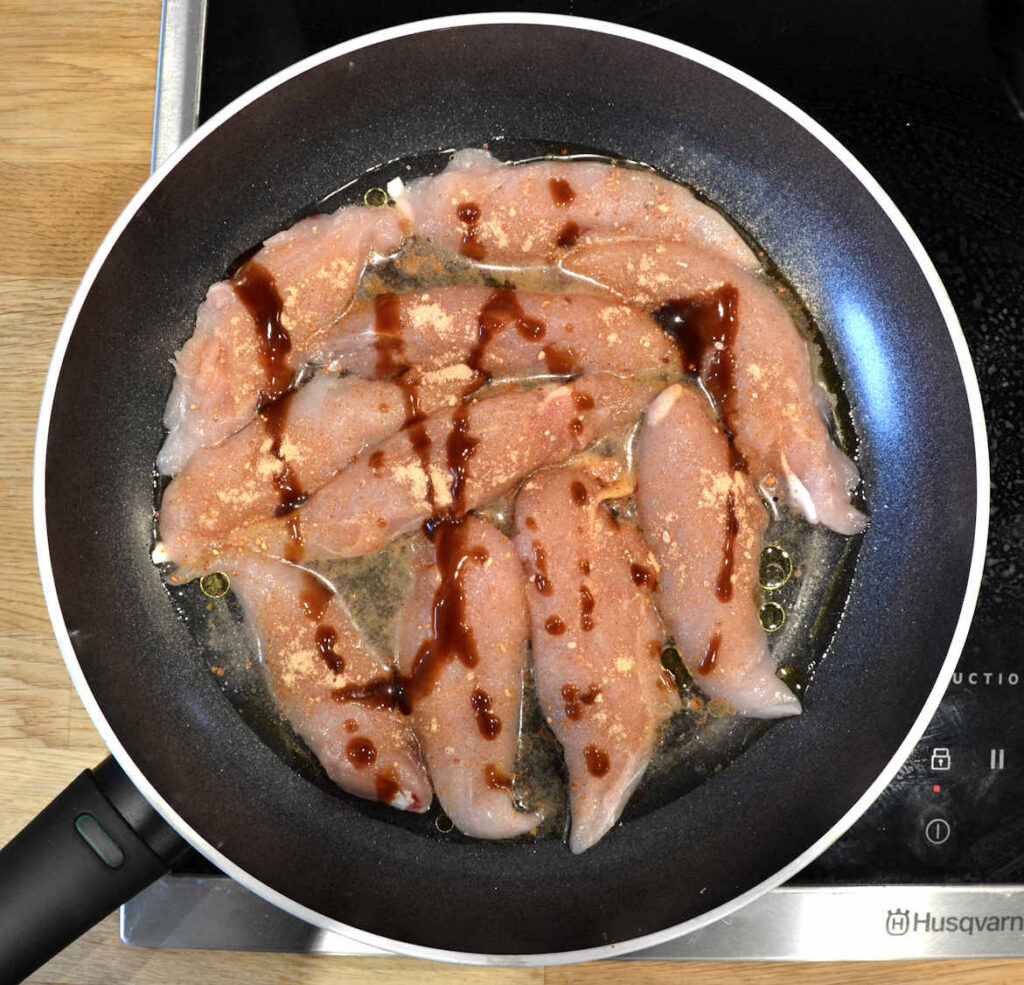 The chicken, with all the added spices, in a pan.