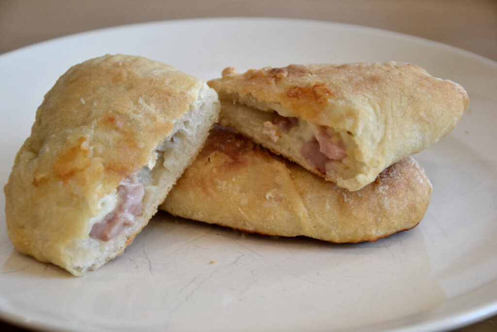 Calzoni on plate. One Calzone, filled with melted cheese and ham, is split in half.
