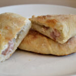 Calzoni on plate. One Calzone, filled with melted cheese and ham, is split in half.